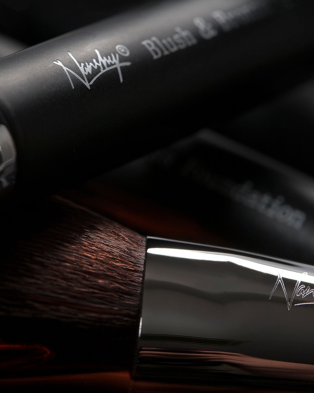 Close-up of Nanshy Gobsmack Glamorous makeup brushes with sleek black handles and shiny metallic ferrules.